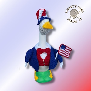 May include: A crocheted goose figurine dressed as Uncle Sam, complete with a red, white, and blue top hat, a blue jacket, and a red bow tie. The goose holds a small American flag. The text "KNOTTY GIRL MADE IT" is in the upper right corner.