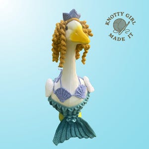 K&ouml;nnte beinhalten: Eine skurrile G&auml;nsefigur als Meerjungfrau verkleidet. Die Gans tr&auml;gt einen geh&auml;kelten Muschel-Bikini, eine blaue Krone und lockiges gelbes Haar. Die Meerjungfrauenschwanzflosse ist t&uuml;rkis. Das Logo "Knotty Girl Made It" ist zu sehen.