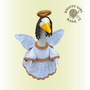 May include: A whimsical goose figurine dressed as an angel, complete with a halo and wings. The goose wears a white crochet outfit with gold trim. The image includes the text "KNOTTY GIRL MADE IT".