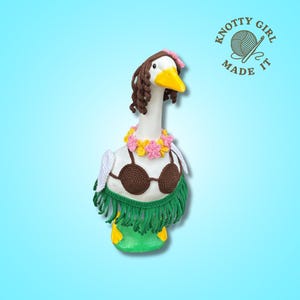 May include: A handcrafted goose figurine, adorned with a brown crochet bikini top, a green fringe skirt, and a floral lei. The goose wears a brown wig and a pink flower. The text "KNOTTY GIRL MADE IT" is in the upper right corner.