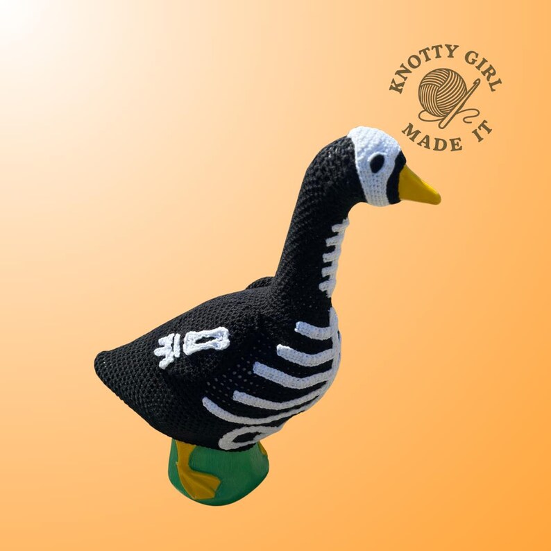K&ouml;nnte beinhalten: Eine handgefertigte H&auml;kelgans in Schwarz mit wei&szlig;en Skelett-Details. Die Gans hat einen wei&szlig;en Kopf, einen gelben Schnabel und steht auf einer gr&uuml;nen Basis. Das Bild enth&auml;lt den Text "Knotty Girl Made It".