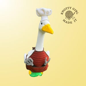 May include: A white goose figurine with a yellow beak and a white chef's hat. The goose wears a red crocheted apron with gray and white oven mitts. The text "KNOTTY GIRL MADE IT" is in a circle on the right.