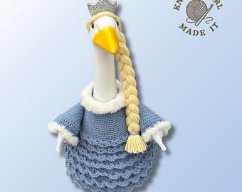 Könnte beinhalten: Eine gehäkelte Gänsepuppe mit blauem Kleid mit weißer Bordüre, silberner Krone und langem blondem Zopf. Die Gans hat einen gelben Schnabel und steht vor einem hellblauen Hintergrund. Der Text "Knotty Girl Made It" befindet sich oben rechts.