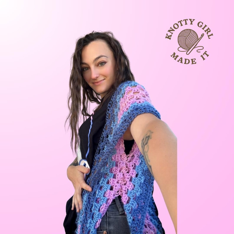 Pode incluir: Um xale de croch&ecirc; feito &agrave; m&atilde;o em tons de azul e rosa. O design vazado apresenta um decote em V e uma fenda frontal. A imagem inclui o texto "Knotty Girl Made It".