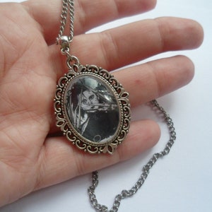 May include: A silver chain necklace with a silver oval pendant featuring a black and white image of a woman's face.