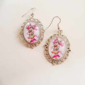 Könnte beinhalten: Silberne Ohrringe mit einem rosa und weißen Anime-Charakter in einer Kamee.