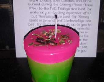 May include: A two-toned candle with a pink top and green base, adorned with dried herbs. A white paper with text is in the background. The candle has a lit wick.