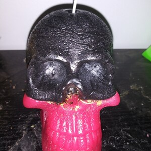 May include: A black and red skull-shaped candle with a wick. The top of the skull is black, and the jaw is red. The candle is on a dark surface.