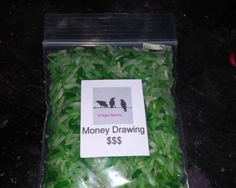 May include: A clear plastic bag filled with green-colored rice. A white label on the bag reads "Money Drawing $$$" with a graphic of three ravens. The rice has a glittery appearance.