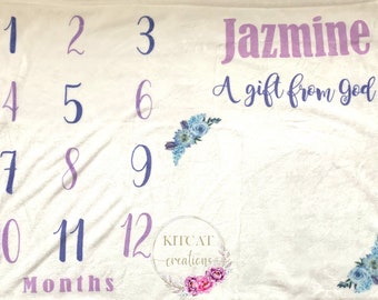May include: A white baby milestone blanket with purple and blue floral designs. The blanket has numbers 1 through 12 printed on it, along with the text "Jazmine A gift from god" and "Months".