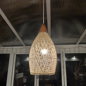 May include: A woven wicker pendant light fixture with a brown wooden top and a white cord hanging from the ceiling.