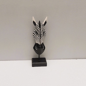 May include: Black and white zebra head sculpture on a black stand. The zebra head is made of wood and has a realistic design.