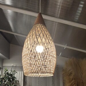 May include: A woven wicker pendant light fixture with a teardrop shape hangs from a white cord. The light fixture is made of natural materials and has a warm, inviting aesthetic.