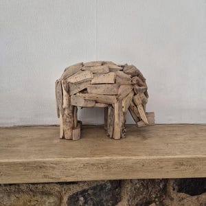Pu&ograve; includere: Una scultura di elefante in legno fatta a mano. L'elefante &egrave; costruito con piccoli pezzi rettangolari di legno di deriva, che gli conferiscono un aspetto strutturato. La scultura ha quattro zampe, un corpo arrotondato e una proboscide. &Egrave; esposta su una mensola di legno.