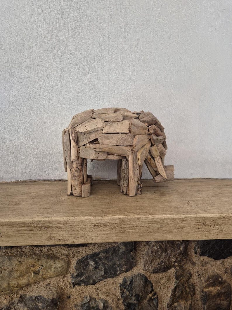 Pu&ograve; includere: Una scultura di elefante in legno fatta a mano. L'elefante &egrave; costruito con piccoli pezzi rettangolari di legno di deriva, che gli conferiscono un aspetto strutturato. La scultura ha quattro zampe, un corpo arrotondato e una proboscide. &Egrave; esposta su una mensola di legno.