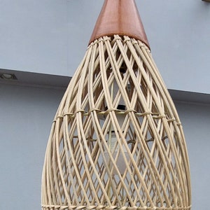 May include: A woven wicker pendant light with a brown wooden top. The light is hanging from a white cord.