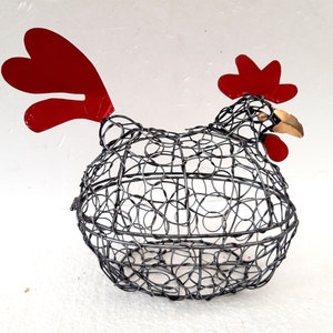 May include: Wire chicken egg holder with a red comb and wattle. The holder is made of wire and has a round shape. It is a decorative item for the kitchen.