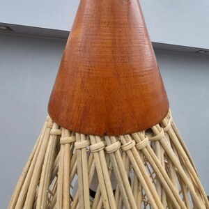 May include: A woven wicker pendant light with a brown wooden cone-shaped top. The light is hanging from a white cord.