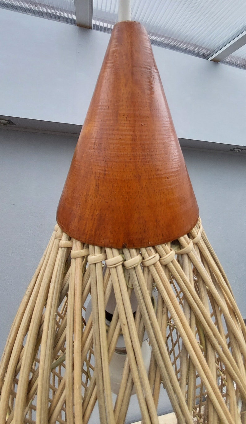 May include: A woven wicker pendant light with a brown wooden cone-shaped top. The light is hanging from a white cord.