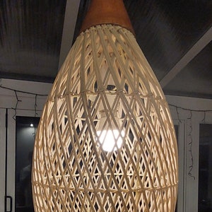 May include: A woven wicker pendant light with a brown top and a white cord hanging from the ceiling. The light is on and illuminates the room.