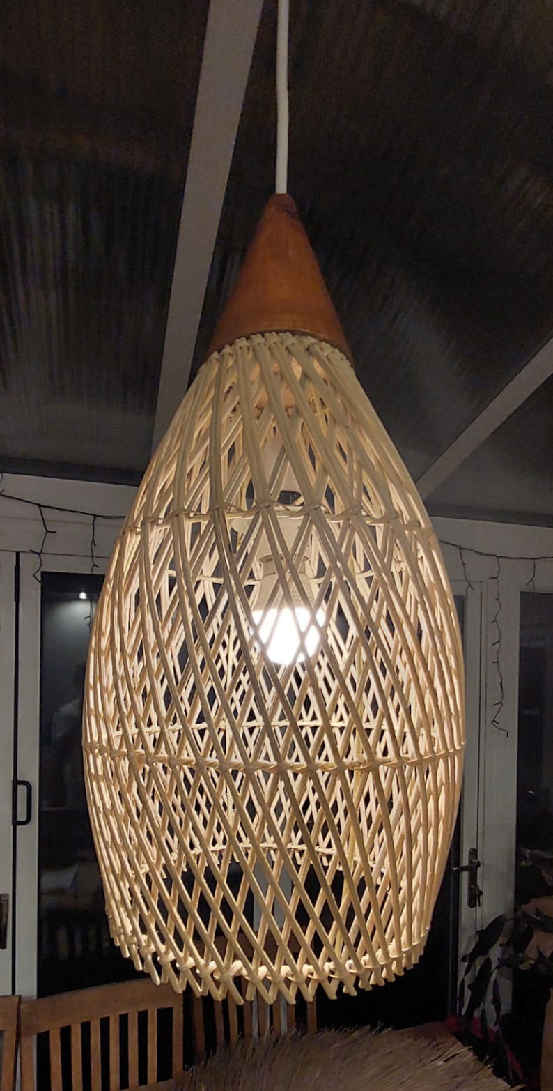 May include: A woven wicker pendant light with a brown top and a white cord hanging from the ceiling. The light is on and illuminates the room.