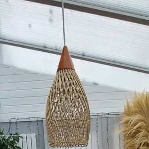 May include: A woven wicker pendant light with a brown wooden top. The light is hanging from a white cord.