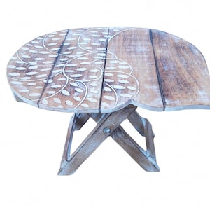 May include: A small, wooden folding table with a white painted design of leaves and dots. The table is in a light brown colour and has a unique, curved shape.