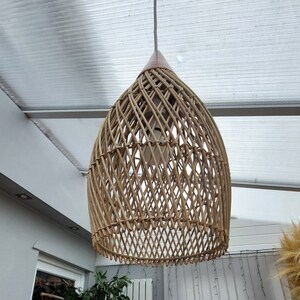 May include: A woven wicker pendant light fixture with a natural brown color. The light fixture is hanging from a white ceiling.