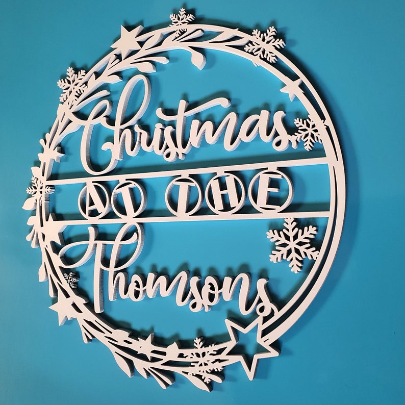 Peut inclure: Guirlande de No&euml;l en bois blanc avec le texte "Christmas at the Thompsons" et un motif de flocon de neige.