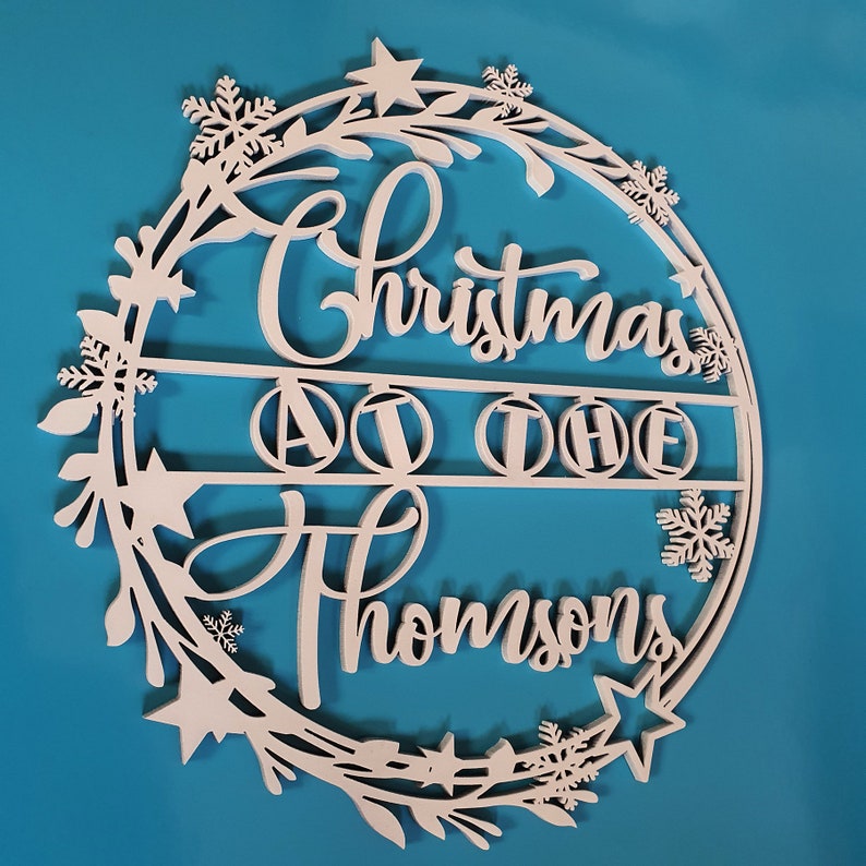 Peut inclure: Guirlande de No&euml;l en bois blanc avec le texte "Christmas at the Thompsons" et un design de guirlande d&eacute;coratif.