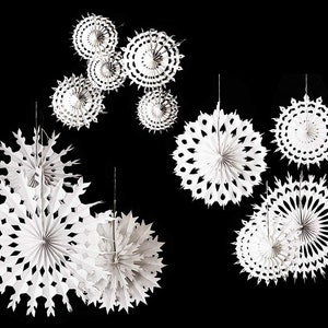 May include: White paper snowflake decorations of various sizes hang against a black background. The decorations have intricate cut-out designs, resembling snowflakes and circular patterns. These festive ornaments are ideal for holiday or winter-themed decor.