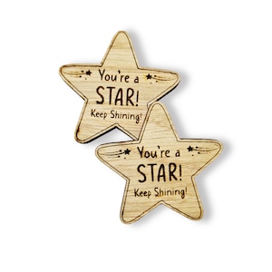 Może przedstawiać: Dwa drewniane żetony w kształcie gwiazdy z wygrawerowanym tekstem "You're a STAR! Keep Shining!"