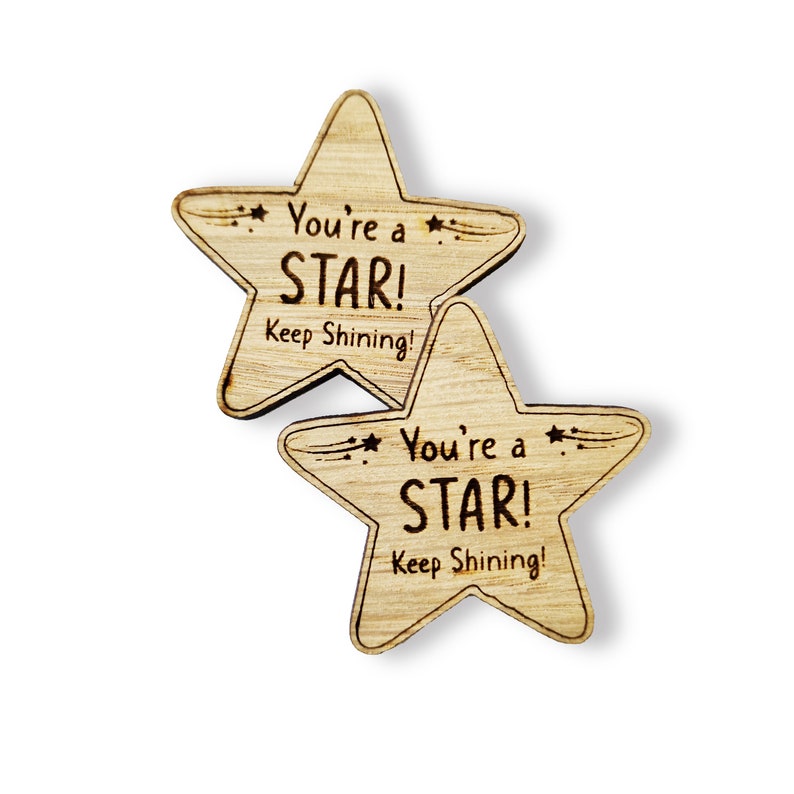 Może przedstawiać: Dwa drewniane żetony w kształcie gwiazdy z wygrawerowanym tekstem "You're a STAR! Keep Shining!"