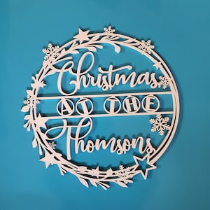 Peut inclure: Guirlande de No&euml;l en bois blanc avec le texte "Christmas at the Thompsons" et un motif de flocon de neige.