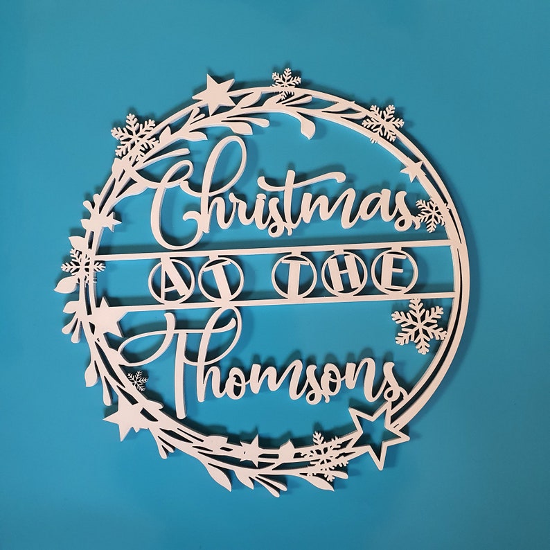 Peut inclure: Guirlande de No&euml;l en bois blanc avec le texte "Christmas at the Thompsons" et un motif de flocon de neige.