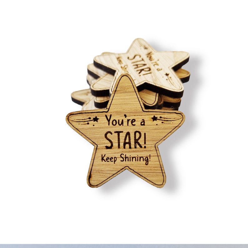 Może przedstawiać: Stos drewnianych gwiazdek z wygrawerowanym tekstem "You're a STAR! Keep Shining!"