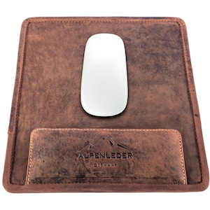 May include: A brown leather mouse pad with a stitched pocket and the text "ALPENLEDER GERMANY" embossed on the front. A white wireless mouse is sitting on the pad.