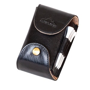 Könnte beinhalten: Ein schwarzer Leder-Golfteehalter mit einem goldenen Knopf und dem geprägten Text "Alpenstock" auf der Vorderseite. Der Halter ist mit weißen Golftees gefüllt.