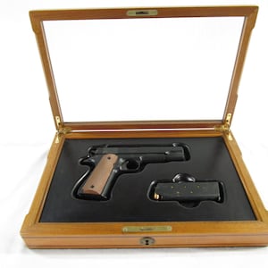 May include: A wooden display case with a glass top, showcasing a black handgun with a brown grip and a black magazine.