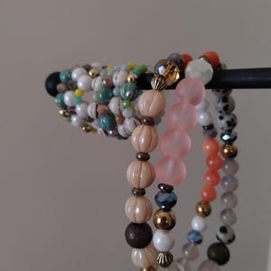 May include: A stack of colorful beaded bracelets with various textures and colors, including white, pink, orange, brown, and turquoise.