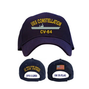 May include: A navy blue baseball cap with the text "USS CONSTELLATION CV-64" embroidered on the front. The back of the cap has the option to personalize with a name and rank or a US flag.