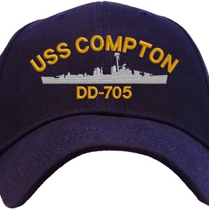 May include: A navy blue baseball cap with an embroidered image of the USS Compton DD-705. The ship's name and number are in gold embroidery.