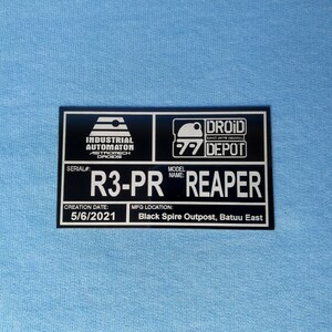 Puede incluir: Placa rectangular negra con texto y logotipos blancos. La placa dice "Industrial Automaton Droids" y "Droid Depot". Tambi&eacute;n muestra "R3-PR REAPER" y "5/6/2021" sobre un fondo azul claro.
