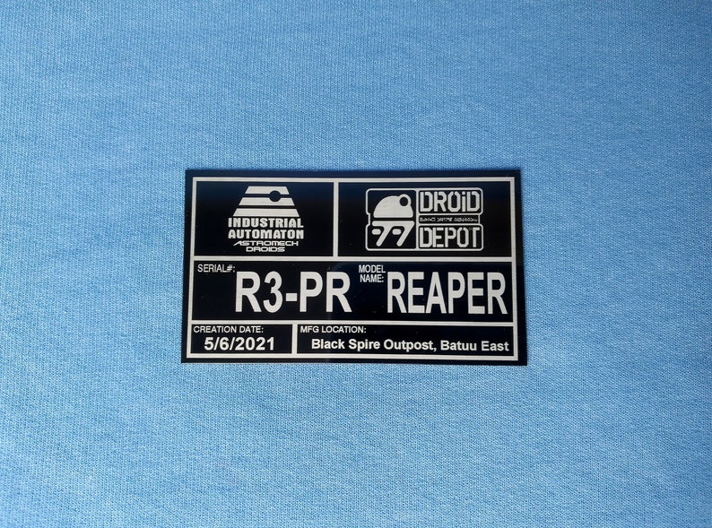 Puede incluir: Placa rectangular negra con texto y logotipos blancos. La placa dice "Industrial Automaton Droids" y "Droid Depot". Tambi&eacute;n muestra "R3-PR REAPER" y "5/6/2021" sobre un fondo azul claro.
