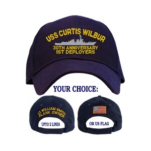 May include: A navy blue baseball cap with the text "USS CURTIS WILBUR 30TH ANNIVERSARY 1ST DEPLOYERS" embroidered on the front. The back of the cap has the option of a personalized embroidered name or the American flag.