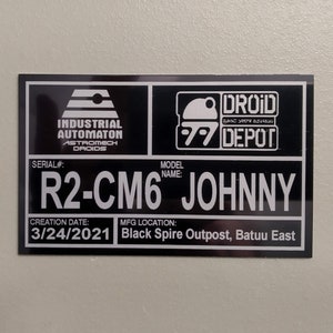 Puede incluir: Un letrero rectangular en blanco y negro con el texto "INDUSTRIAL AUTOMATON ASTROMECH DROIDS" y "DROID DEPOT". El letrero incluye el n&uacute;mero de serie "R2-CM6" y el nombre del modelo "JOHNNY". La fecha de creaci&oacute;n es el 24/03/2021 y el lugar de fabricaci&oacute;n es Black Spire Outpost, Batuu East.