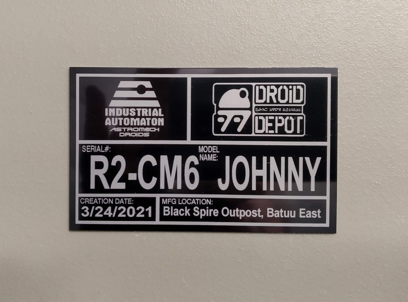 Puede incluir: Un letrero rectangular en blanco y negro con el texto "INDUSTRIAL AUTOMATON ASTROMECH DROIDS" y "DROID DEPOT". El letrero incluye el n&uacute;mero de serie "R2-CM6" y el nombre del modelo "JOHNNY". La fecha de creaci&oacute;n es el 24/03/2021 y el lugar de fabricaci&oacute;n es Black Spire Outpost, Batuu East.