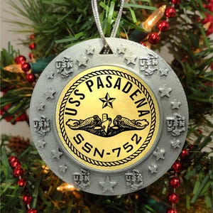 May include: Silver ornament with a gold circle featuring the text "USS PASADENA SSN-752" and a submarine graphic. The ornament is decorated with stars and the letters "USN" around the outer edge.