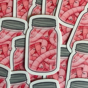 Pode incluir: Uma folha de adesivos com ilustrações de frascos de vidro cheios de minhocas cor-de-rosa. Os adesivos são brancos com uma borda arredondada.