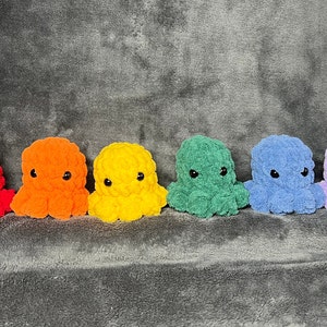 May include: Six crocheted octopus plushies in a rainbow color scheme. The plushies are arranged in a row from left to right: red, orange, yellow, green, blue, and purple.
